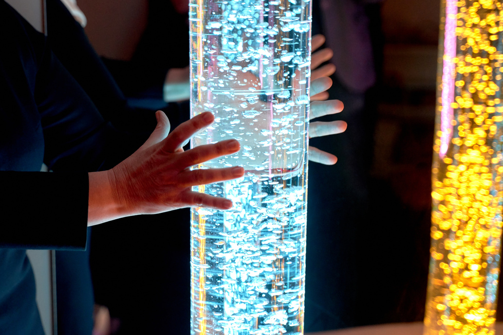 therapy sensory stimulating multi sensory room, woman interacting with colored lights bubble tube lamp during therapy session