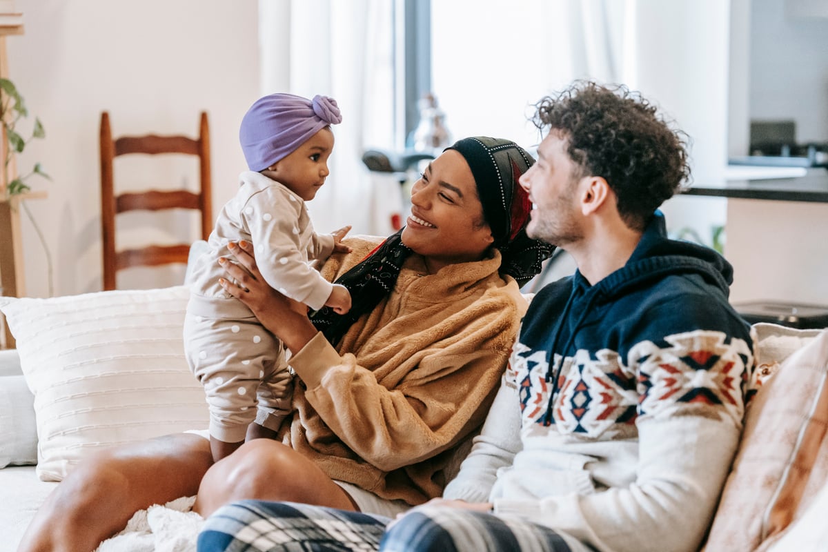 Delight diverse parents sitting on sofa with cute baby